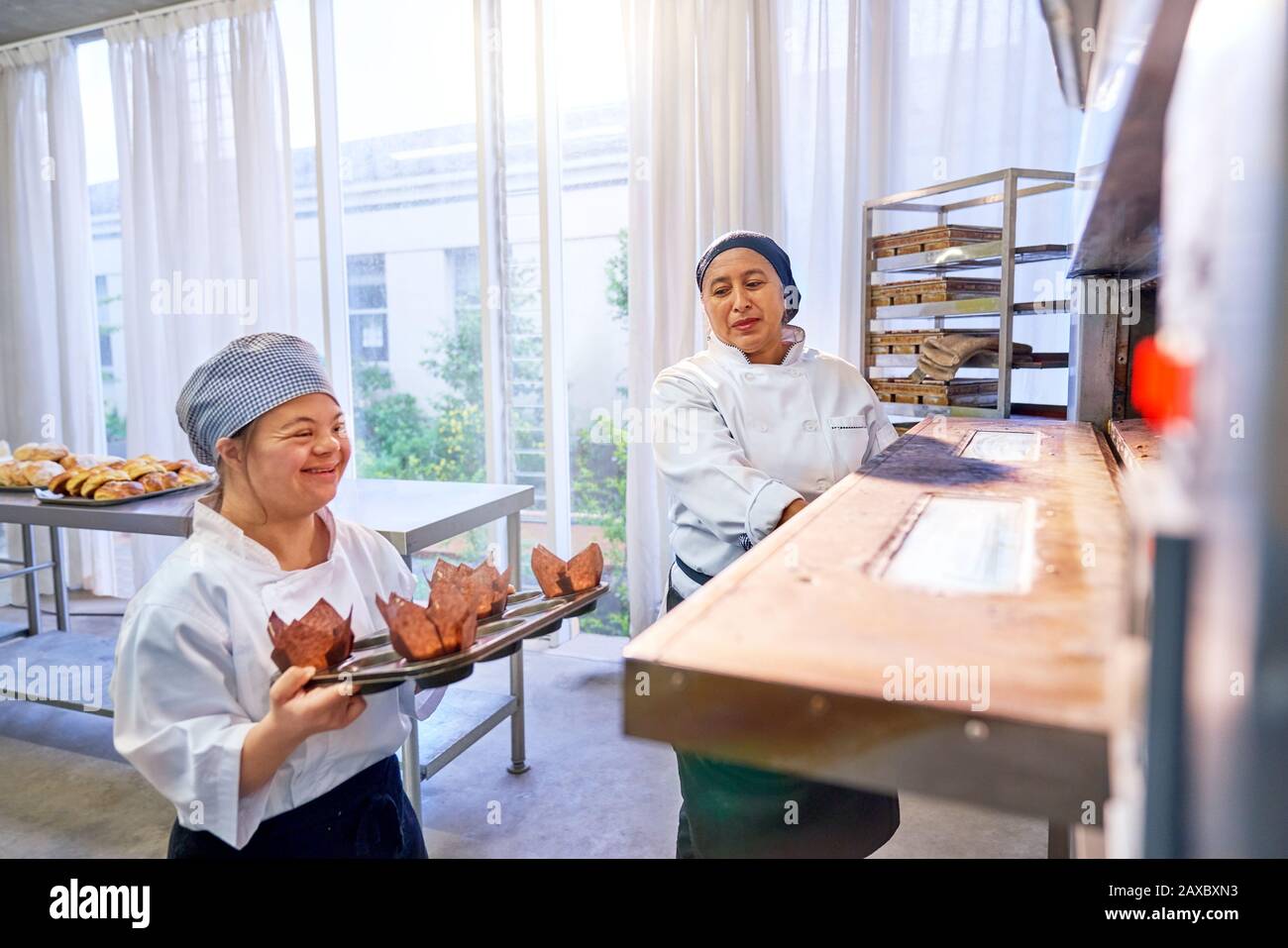Chef et jeune femme avec syndrome De Down plaçant des muffins au four Banque D'Images