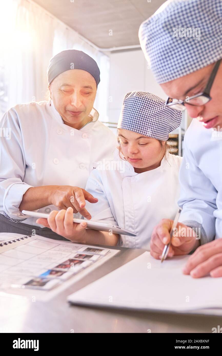 Chef et étudiants avec syndrome De Down utilisant tablette numérique dans la cuisine Banque D'Images