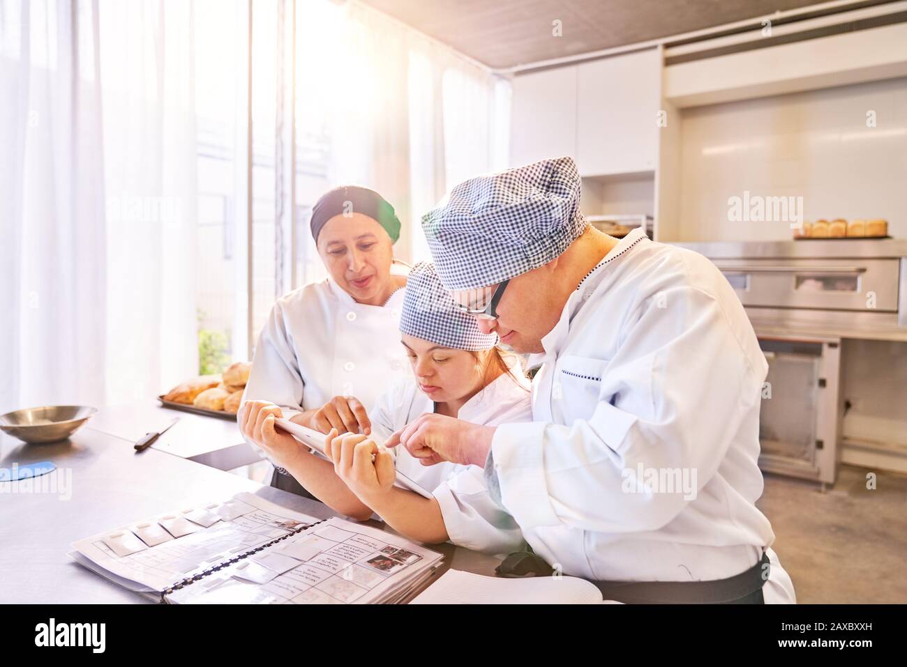 Chef et étudiants avec syndrome De Down utilisant tablette numérique dans la cuisine Banque D'Images