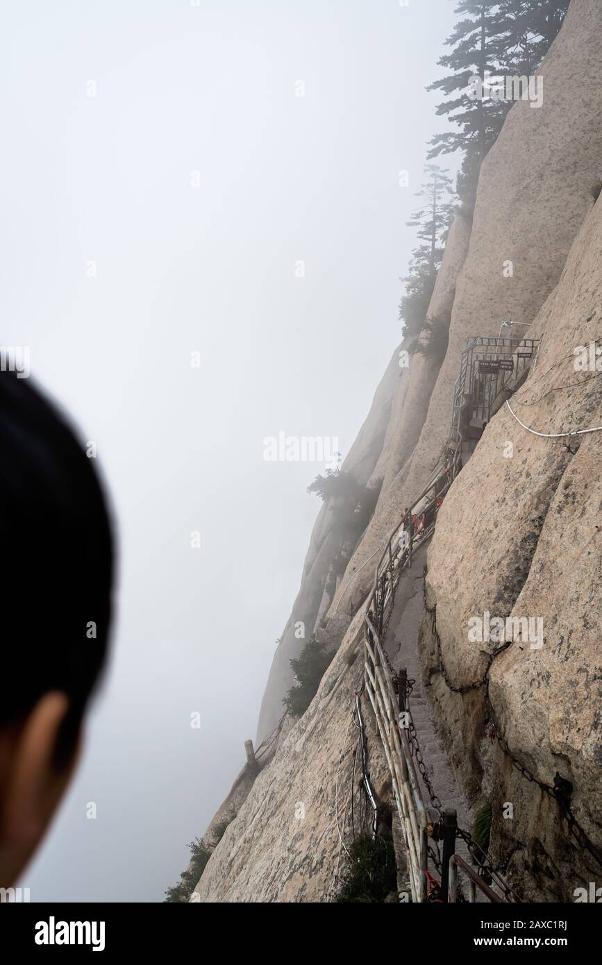 Huashan, Chine - Août 2019 : personne chinoise non identifiée regardant les marches de pierre coupées sur un côté d'un rocher de montagne menant au dangereux et p Banque D'Images
