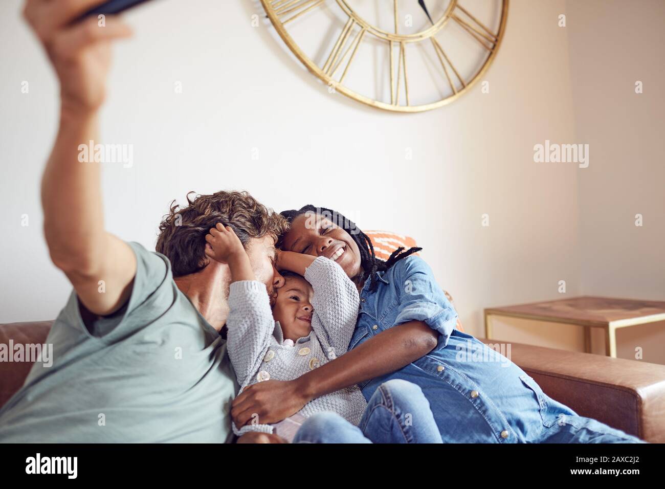 Affectueux jeune famille enceinte prenant selfie sur le canapé salon Banque D'Images