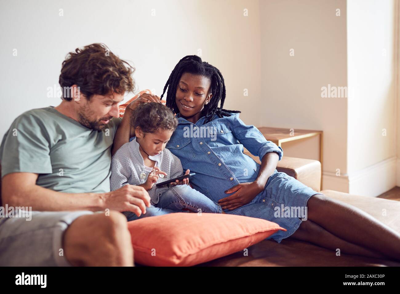 Famille jeune enceinte utilisant un smartphone sur le canapé du salon Banque D'Images