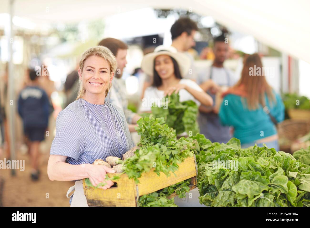 Portrait souriant, femme confiante travaillant, portant une caisse de légumes sur le marché des agriculteurs Banque D'Images