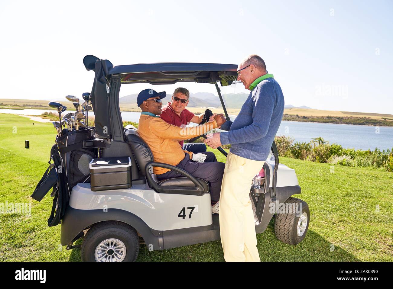 Des amis de golf de sexe masculin parlent à la voiturette de golf sur le terrain de golf ensoleillé Banque D'Images