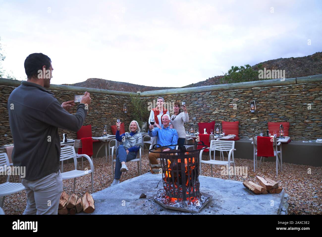 Amis seniors avec vin posant pour la photographie à la cheminée de patio Banque D'Images