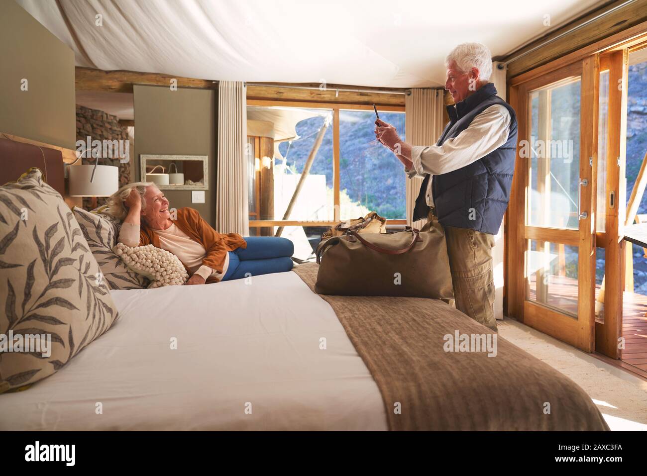 Homme senior avec téléphone caméra photographiant sa femme sur le lit de l'hôtel Banque D'Images