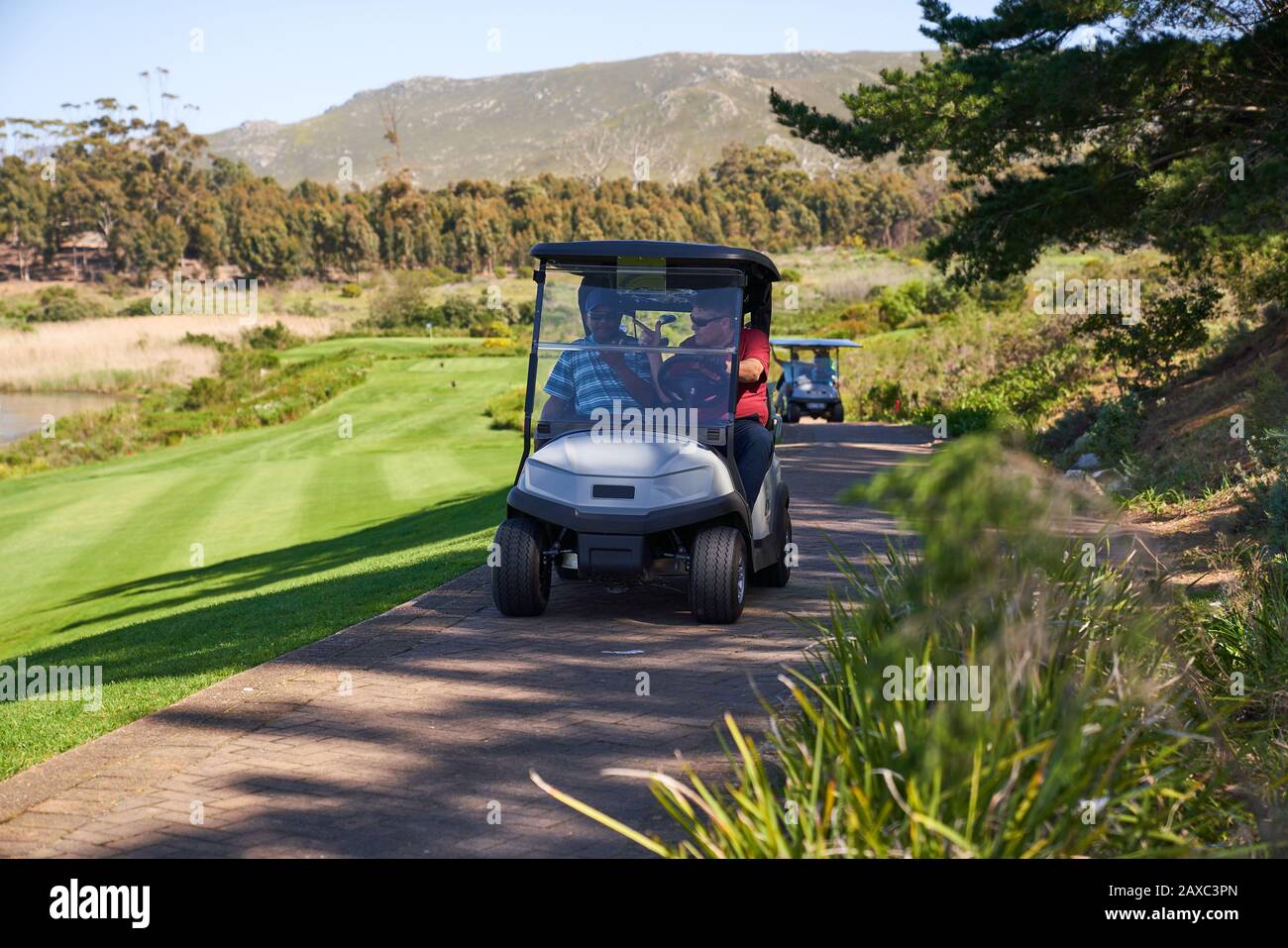 Les golfeurs de sexe masculin qui s'y trouvent dans une voiturette de golf sur un parcours de golf ensoleillé Banque D'Images