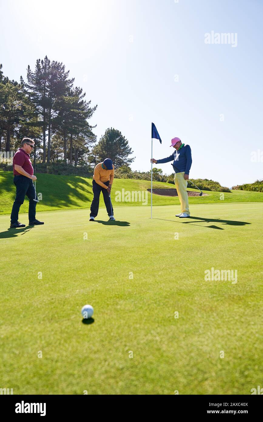 Golf masculin mettant dans le trou sur le terrain de golf ensoleillé vert d'entraînement Banque D'Images