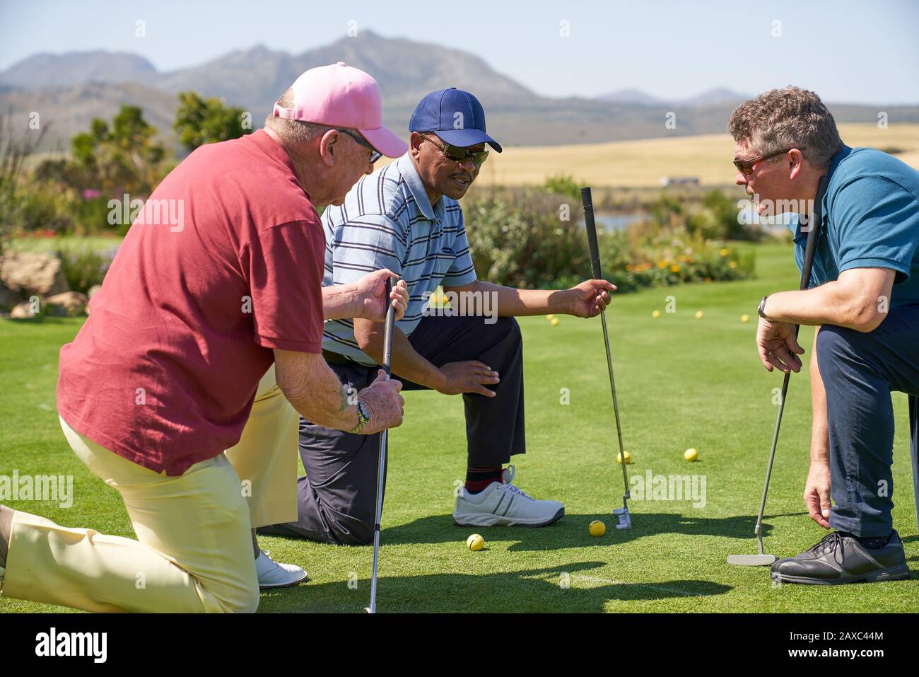 Les golfeurs de sexe masculin s'agenouillent et parlent de vert d'exercice ensoleillé Banque D'Images
