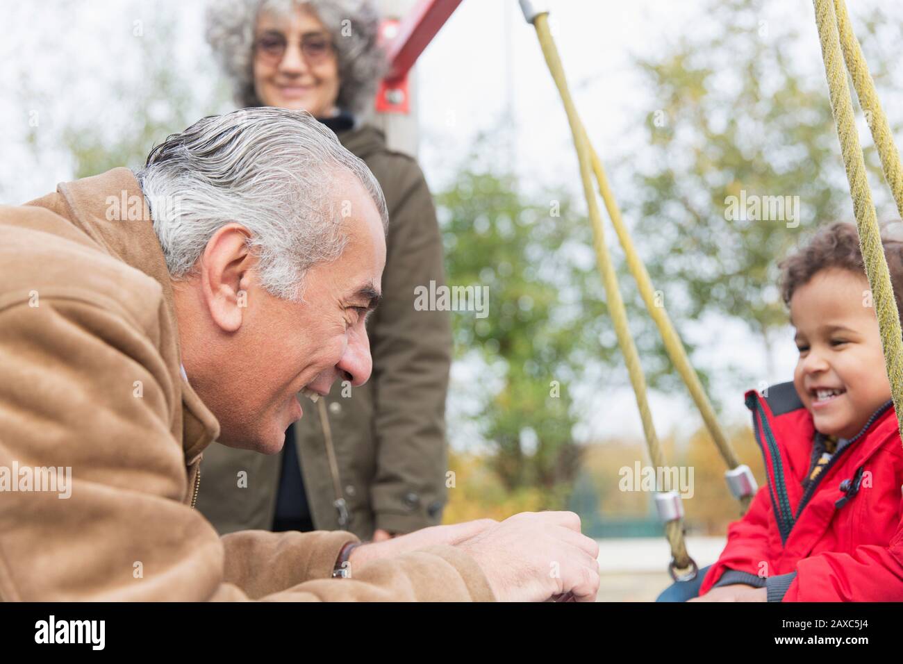 Grand-père jouant avec son petit-fils sur l'oscillation à l'aire de jeux Banque D'Images