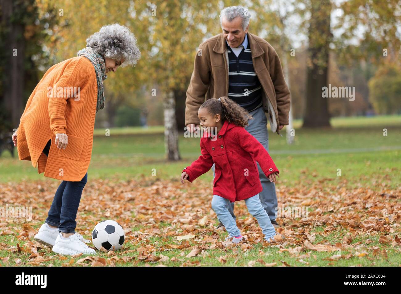 Grands-parents jouant au football avec la petite-fille dans le parc d'automne Banque D'Images