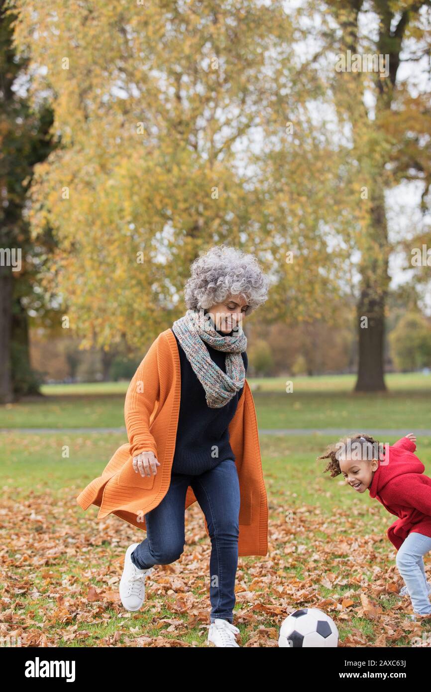 Grand-mère ludique jouant au football avec petite-fille dans le parc d'automne Banque D'Images