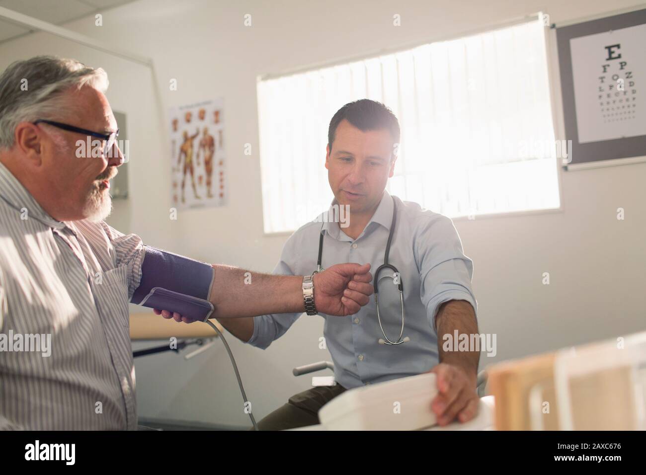 Médecin homme vérifiant la tension artérielle du patient principal dans la salle d'examen Banque D'Images