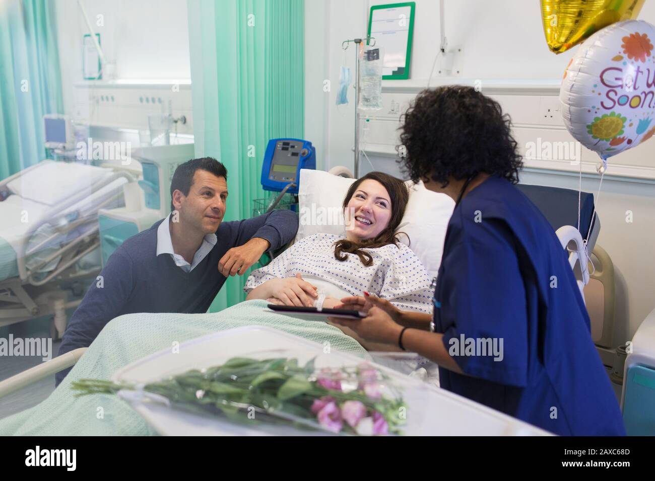 Médecin avec tablette numérique en train de faire des rondes, en parlant avec un couple dans le service hospitalier Banque D'Images