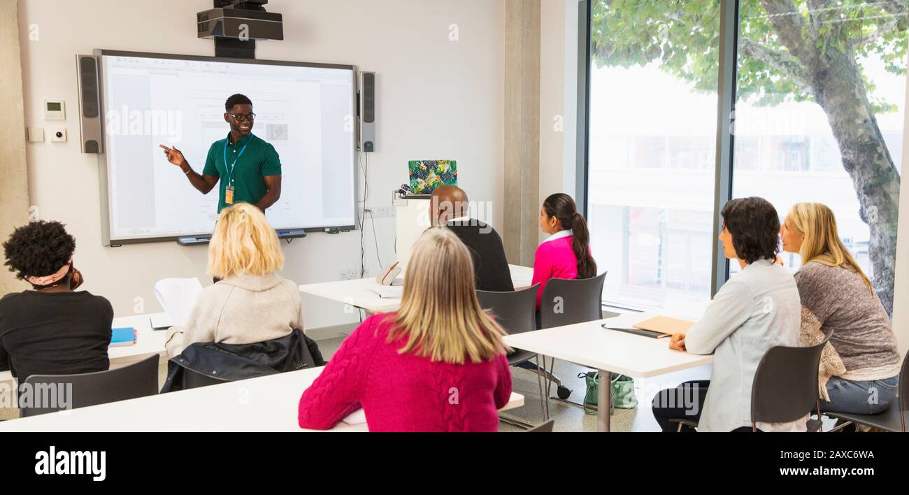 Les étudiants des collèges communautaires qui regardent un instructeur menant une leçon à l'écran de projection en classe Banque D'Images