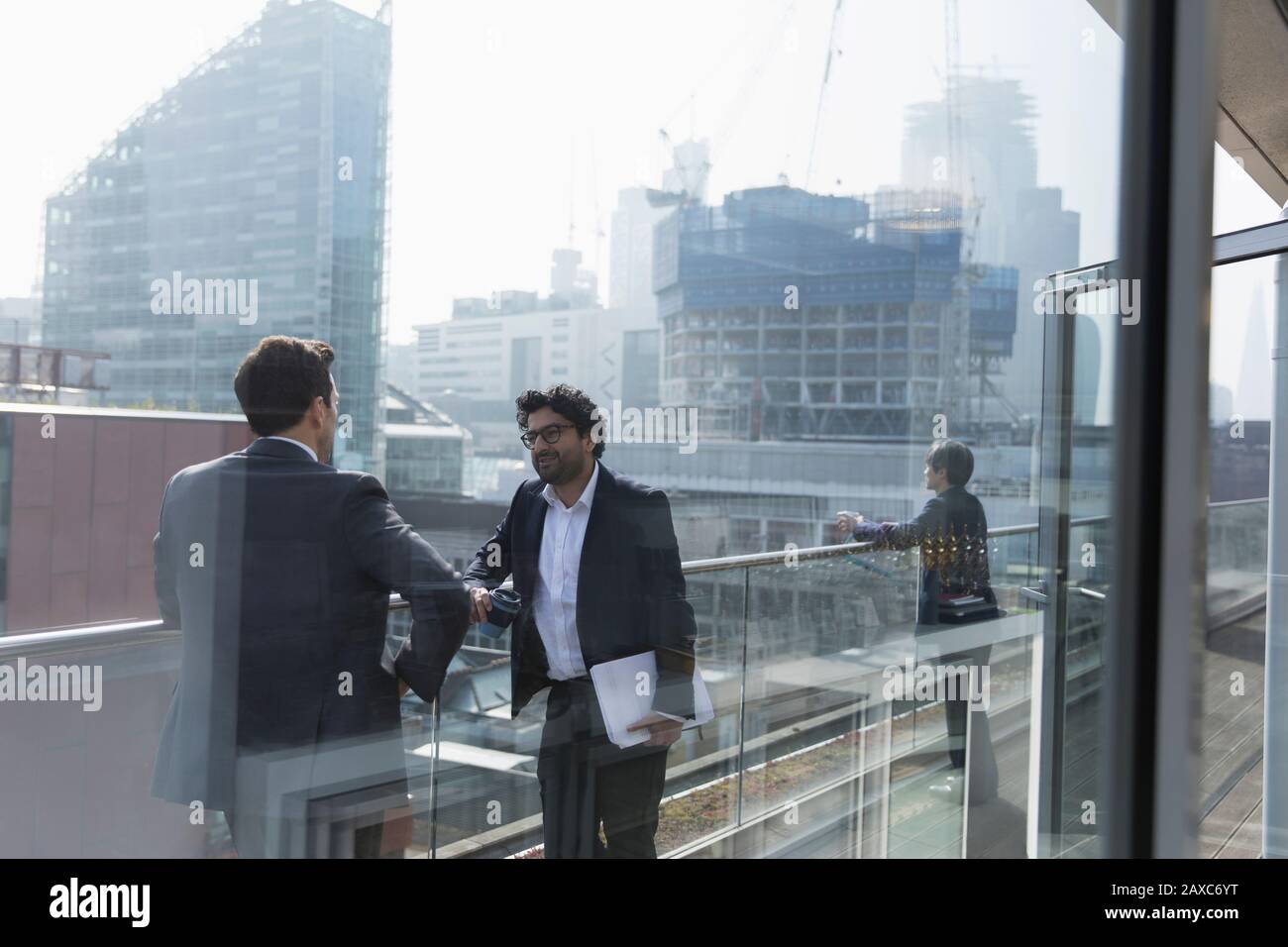 Les hommes d'affaires parlent sur un balcon de bureau ensoleillé et urbain Banque D'Images