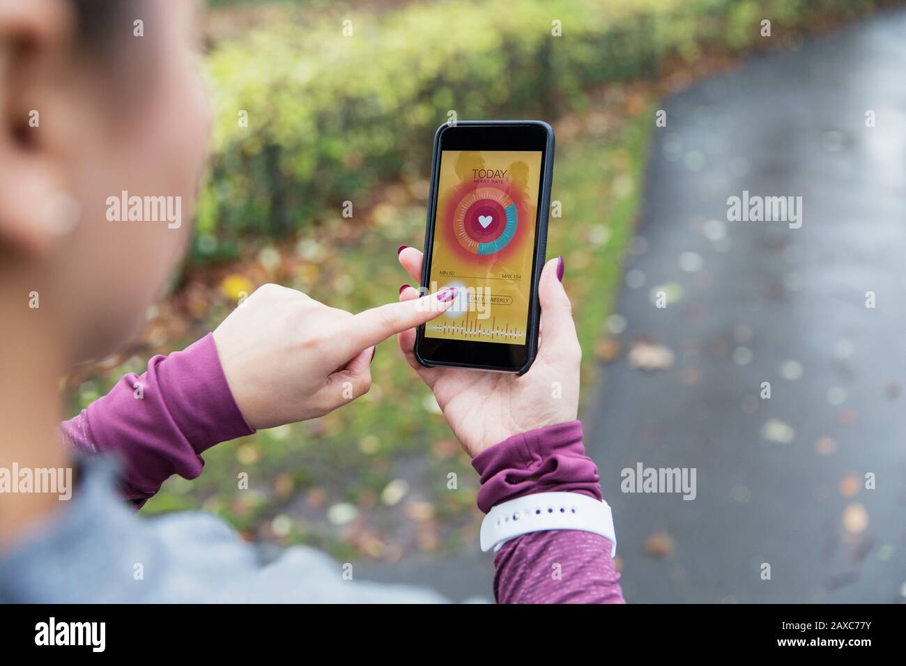 Le coureur femelle contrôle le moniteur de fréquence cardiaque sur le smartphone sur le trajet Banque D'Images