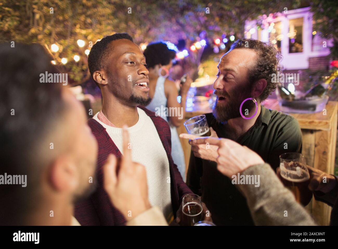 Des amis hommes heureux parlent et boivent à la fête du jardin Banque D'Images
