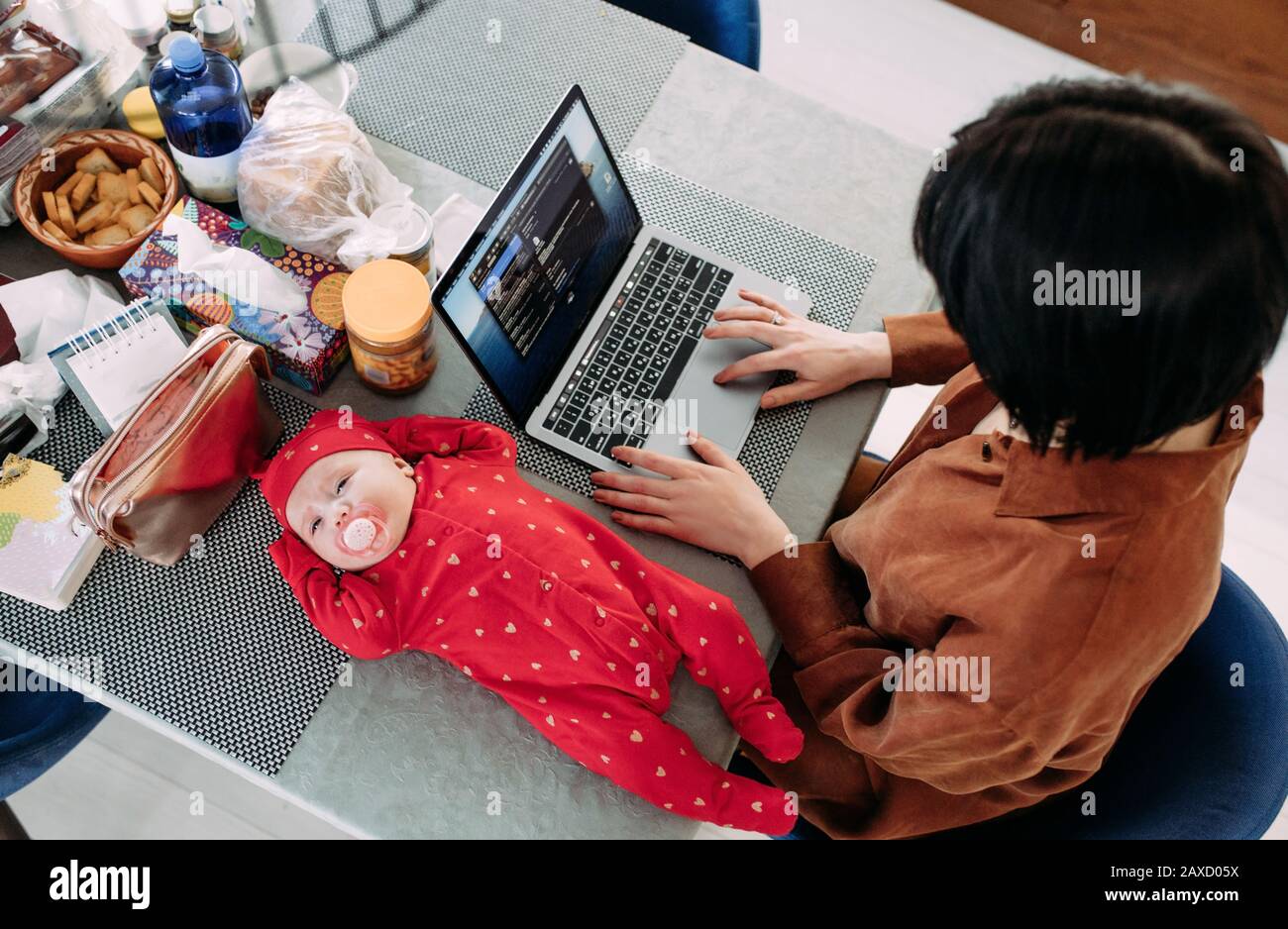 La mère est assise et travaille sur un ordinateur portable près du bébé allongé sur la table. Concept d'emploi des femmes avec des bébés. Vue de dessus. Banque D'Images