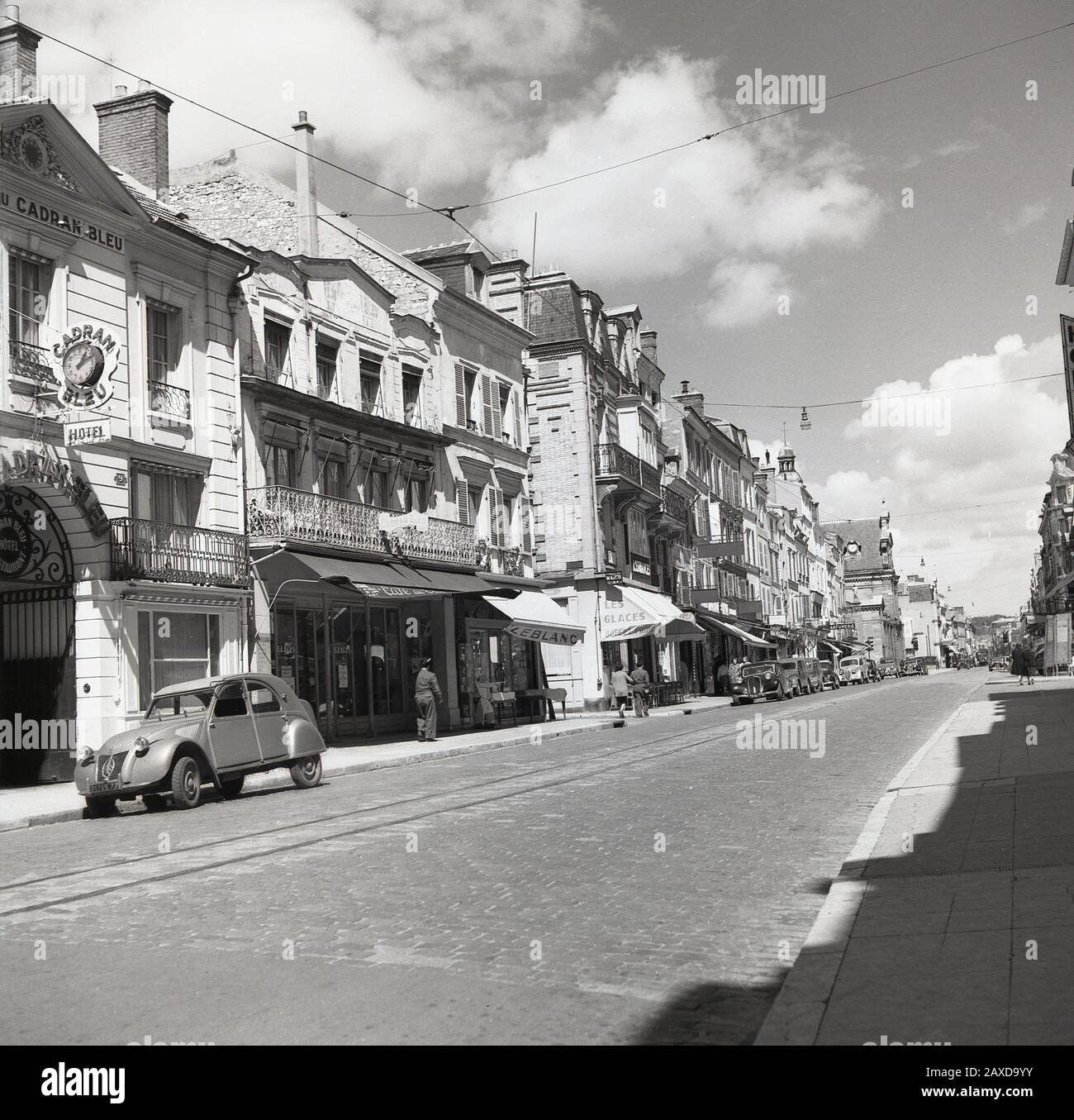 Années 1950, historique, une Citroën 2CV garée à l'extérieur du célèbre Grand Hôtel du cadran Bleu ( l'Hôtel du cadran Bleu) au 77 Fontainebleau, France, une ville de l'historique Château de Fontainebleau, autrefois la maison des rois de France. La 2CV était une voiture économique française produite pour la première fois en 1948 qui est devenue un classique du design. Au milieu de la rue pavée, une voie de tramway. Banque D'Images