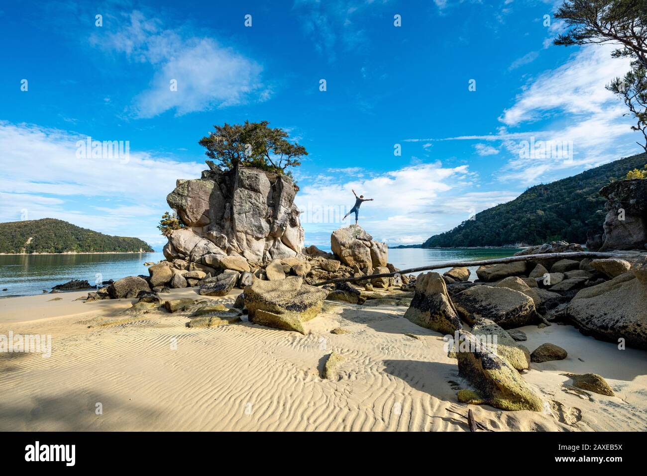 Jeune homme debout avec des bras tendus sur un rocher, roc surcultivé sur la plage de Stillwell Bay, parc national Abel Tasman, Tasman, île du Sud Banque D'Images