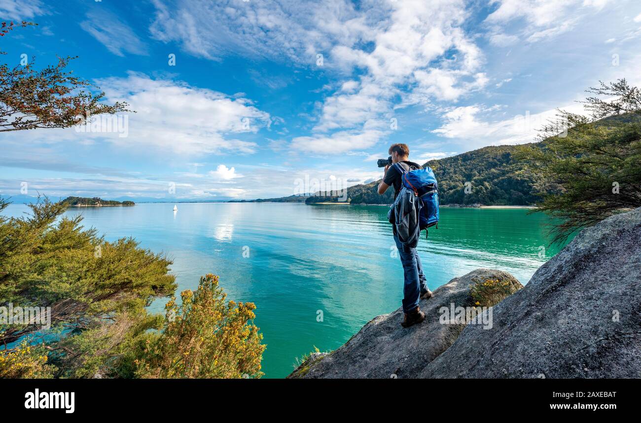 Photographe se tient sur un rocher et prend des photos, Stillwell Bay, Abel Tasman Coastal Track, Abel Tasman National Park, Tasman, South Island, New Banque D'Images