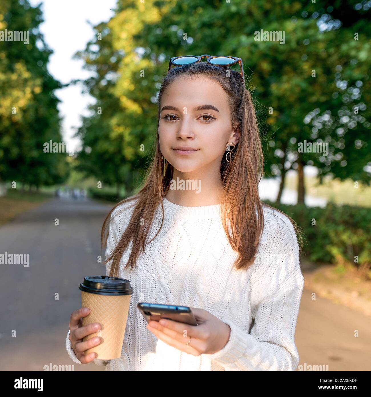 Jeune fille de 10-12 ans, tient smartphone dans sa main, tasse avec thé de café, été sur le parc de rue, beau et pensif. Week-end. Décontracté Banque D'Images