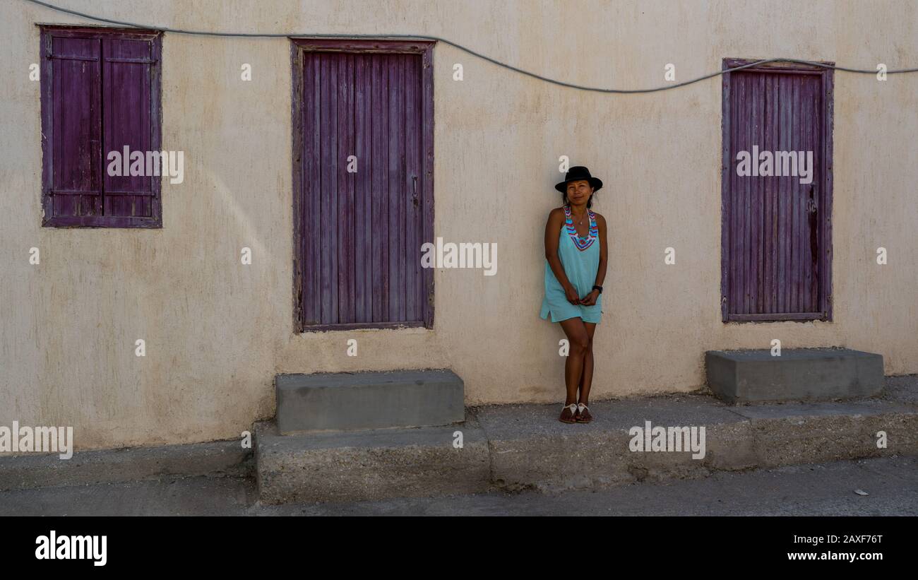 Asian Woman dans des lunettes de soleil et chapeau debout devant la maison grecque traditionnelle avec volets pourpre et portes dans le village d'Eressos sur les îles de Lesv Banque D'Images