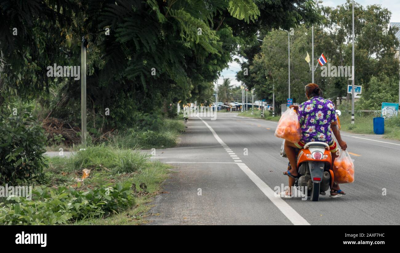 Femme conduite à l'arrière de la moto tenant des sacs en plastique remplis de fruits dans les zones rurales de Pranburi Thaïlande Banque D'Images