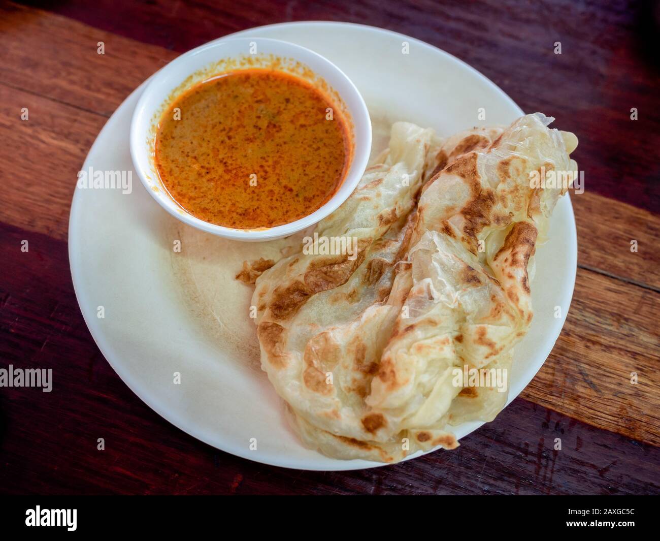 Petit déjeuner de style thaïlandais du sud. Délicieux roti avec curry de lait de coco dans un plat blanc sur table en bois, vue sur le dessus. Banque D'Images