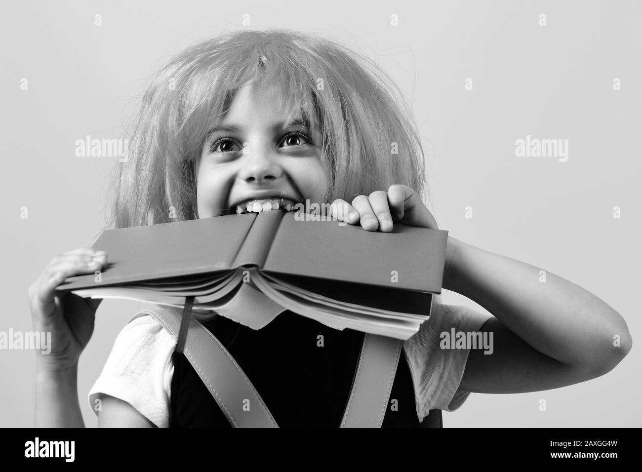 Fille de l'école avec vue heureuse isolée sur fond rose. Retour au concept d'école et d'éducation. Élève en uniforme scolaire avec perruque rose. Fille morde grand livre bleu. Banque D'Images