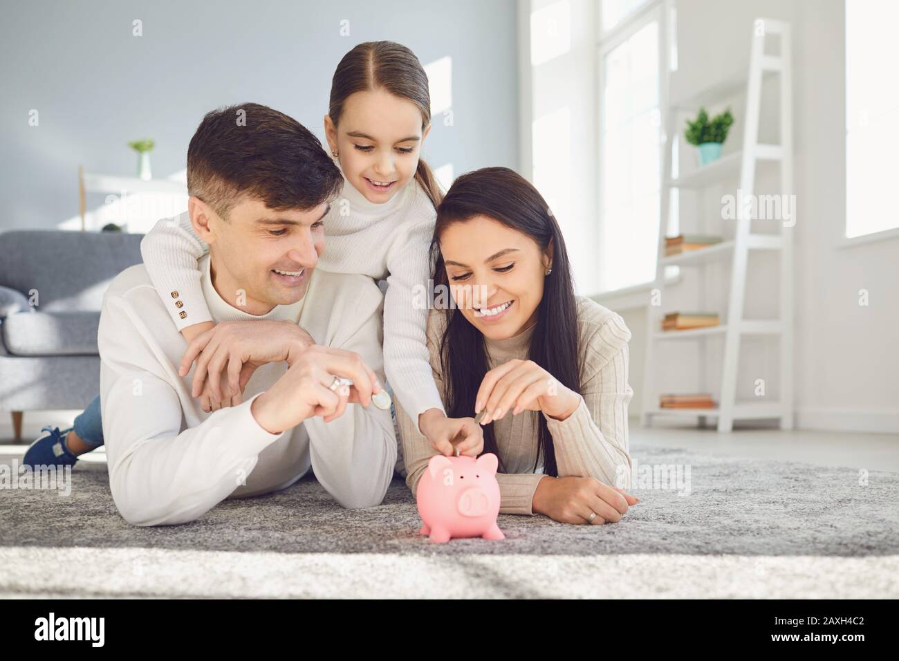 Une famille heureuse économise de l'argent dans un porc de banque piquante. Banque D'Images