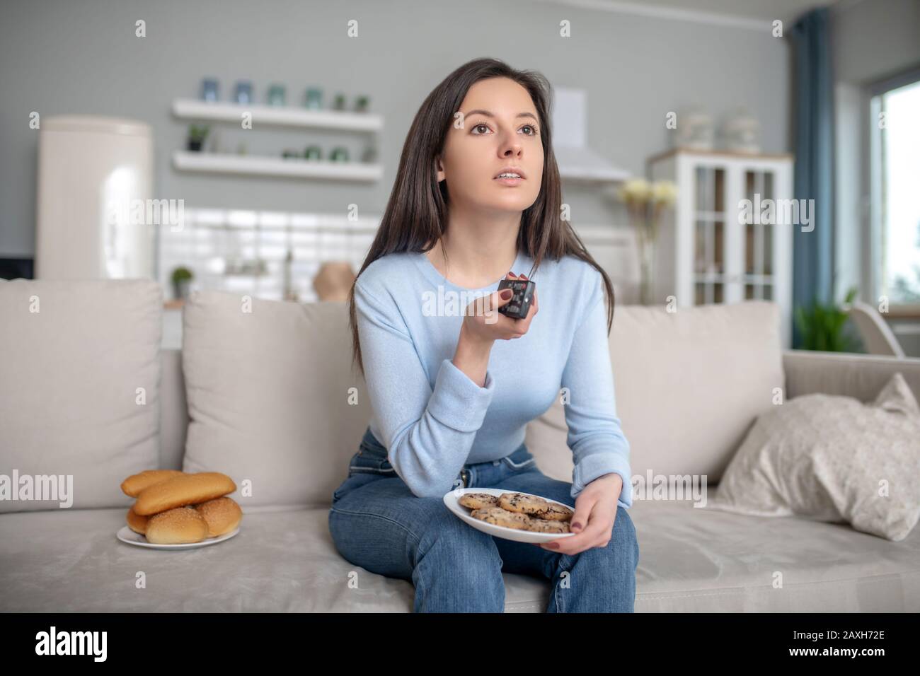 Femme mangeant des cookies et des petits pains près du téléviseur Banque D'Images