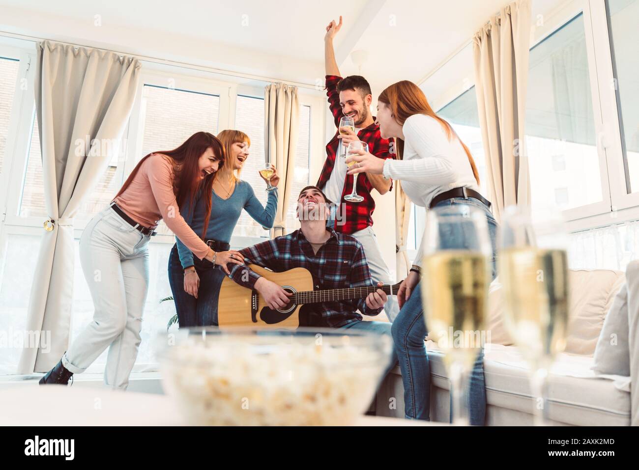 Groupe de jeunes festifs magnifiques qui s'amusent avec du champagne et de la musique à la maison. Banque D'Images