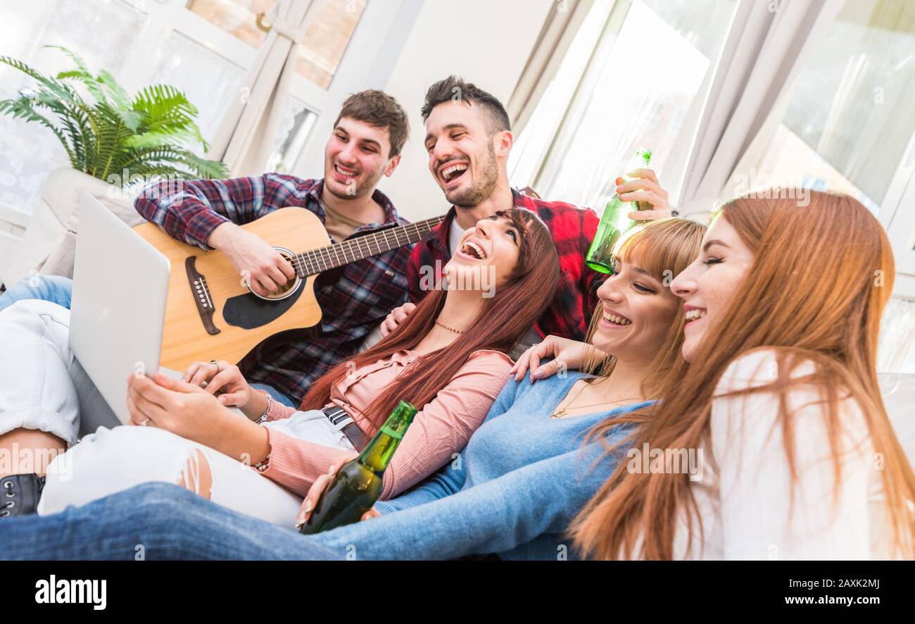 Groupe d'adolescents qui s'amusent à la maison en utilisant un ordinateur portable et en jouant de la guitare dans le salon - Groupe de personnes qui apprécient le temps ensemble Banque D'Images