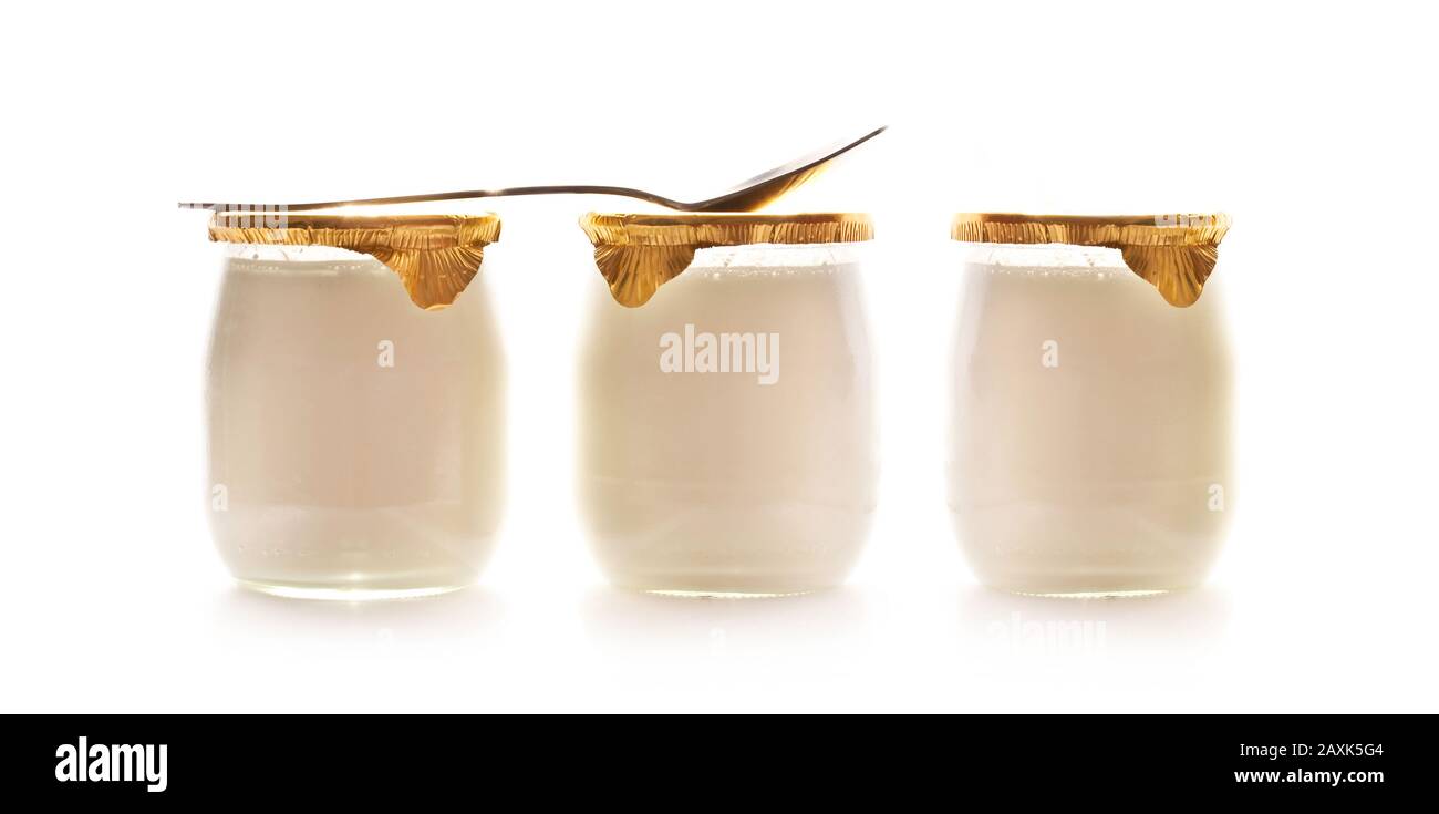 Trois yaourts simples dans des pots en verre et une cuillère isolée sur fond blanc Banque D'Images