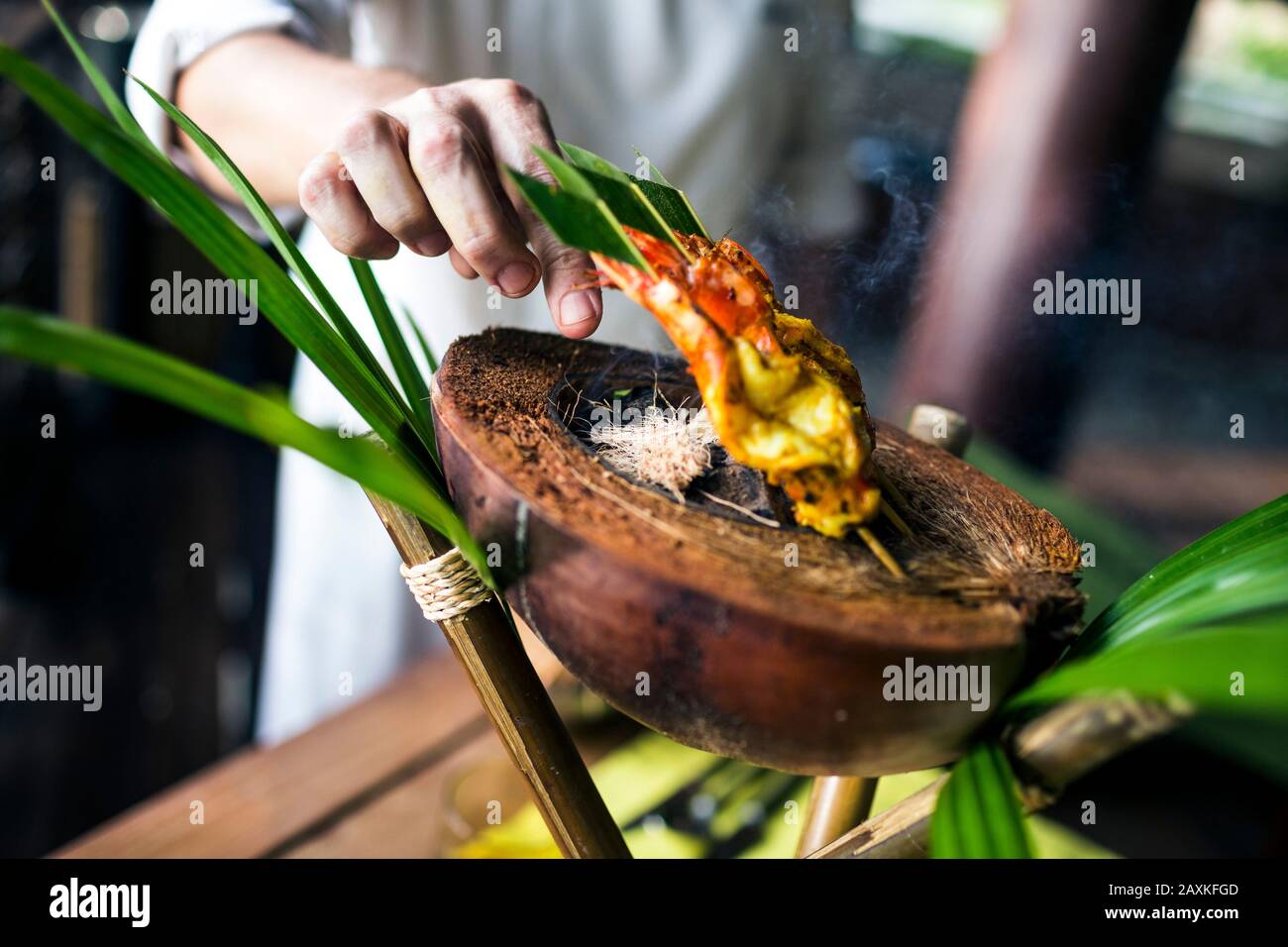 Gros plan du chef préparant du satay de crevette grillé au charbon de bois sur une coquille de noix de coco. Banque D'Images