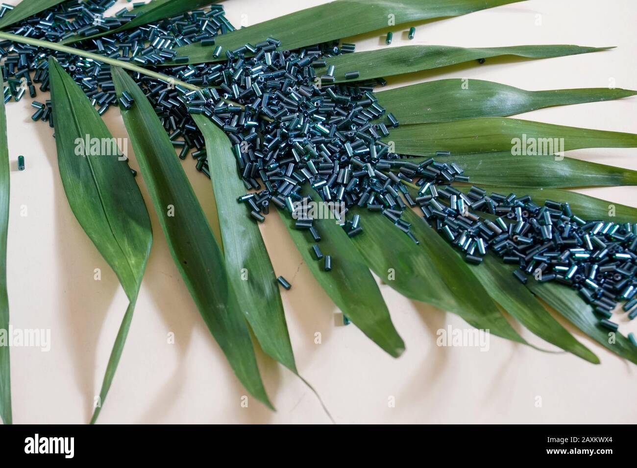 Une multitude de perles tubulaires vertes de toho et de feuilles vertes sur fond crème clair. Perles utilisées pour l'ébélisage de vêtements. Banque D'Images