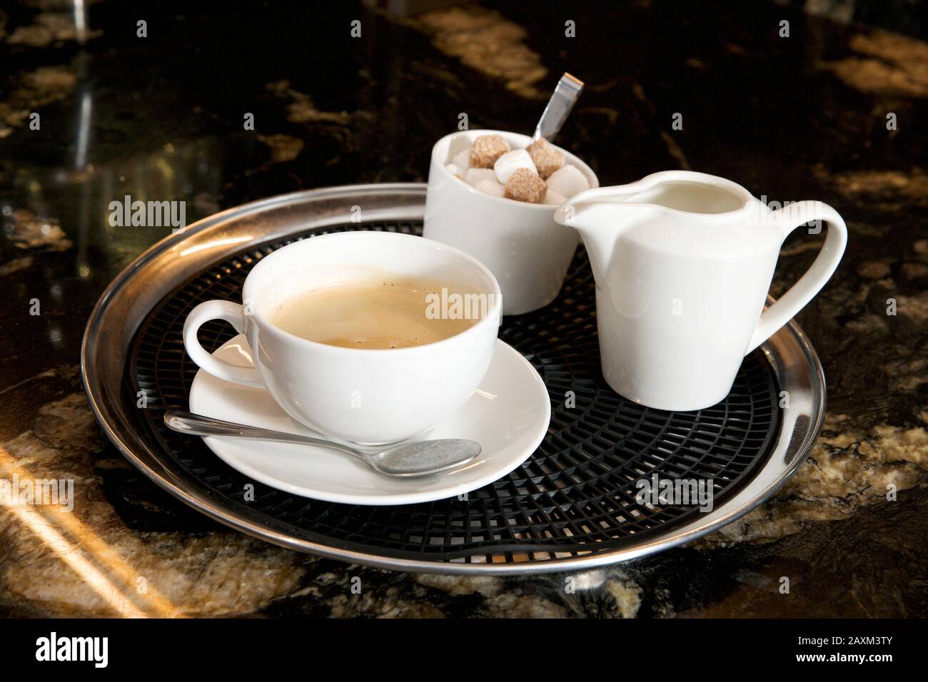 Une tasse de café avec un pot à lait et du sucre sur un plateau sur un comptoir en marbre. Banque D'Images