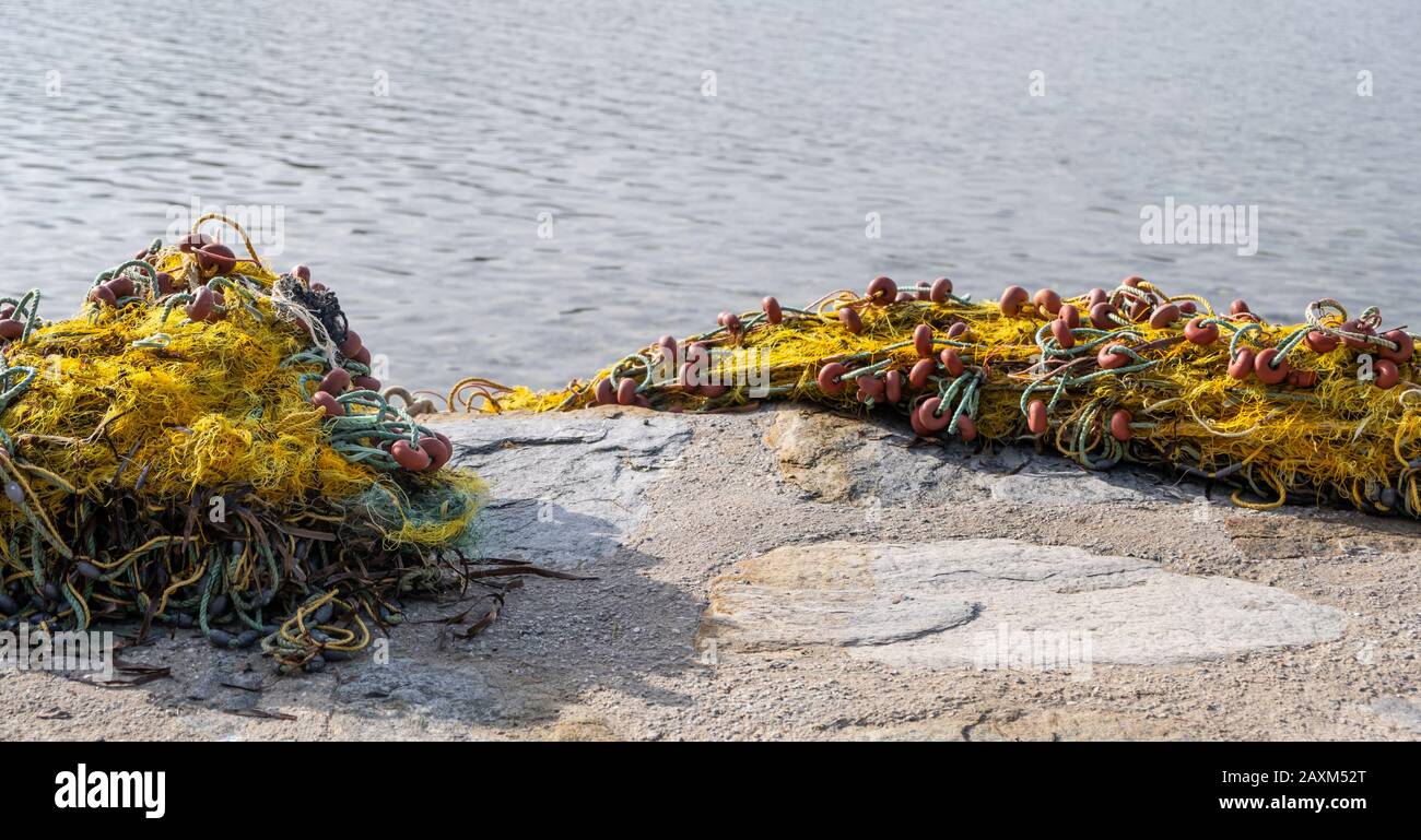 Filets de pêche mis sur terre de ciment pour se sécher. Filets à poisson en nylon jaune avec cordes et corks sous les rayons du soleil et à côté d'un fond bleu calme de mer. Banque D'Images