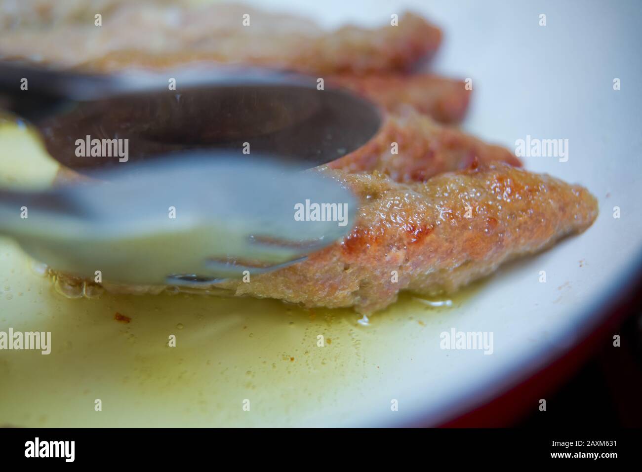 La longue côtelette est frite dans une poêle rouge. Gros plan sur la main d'une femme avec une spatule de cuisine ressemble à une poêle friture frite. Juteux fait maison Banque D'Images