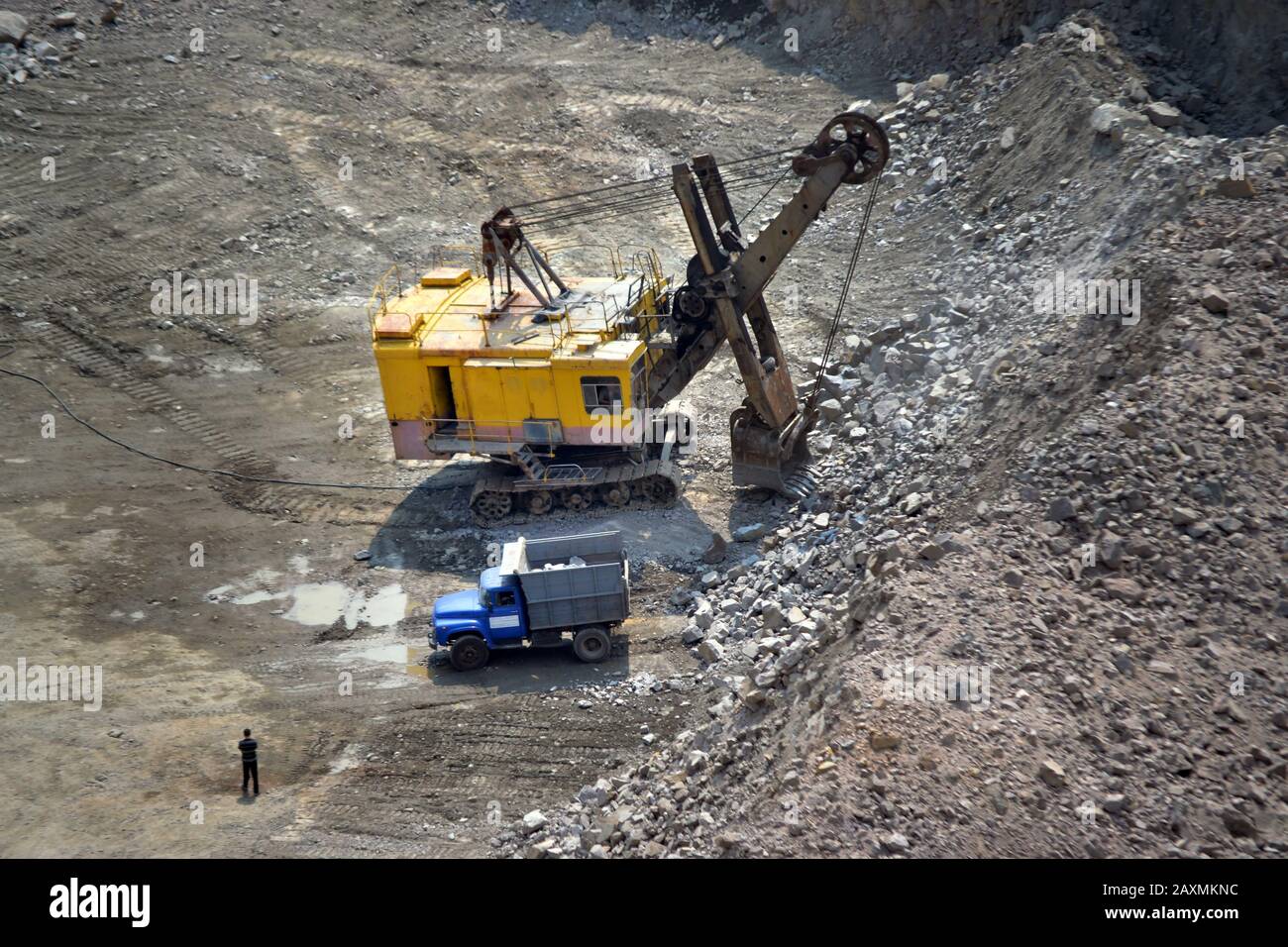 pelle hydraulique, camion et homme de grande taille se tenant à côté d'une carrière de granit Banque D'Images