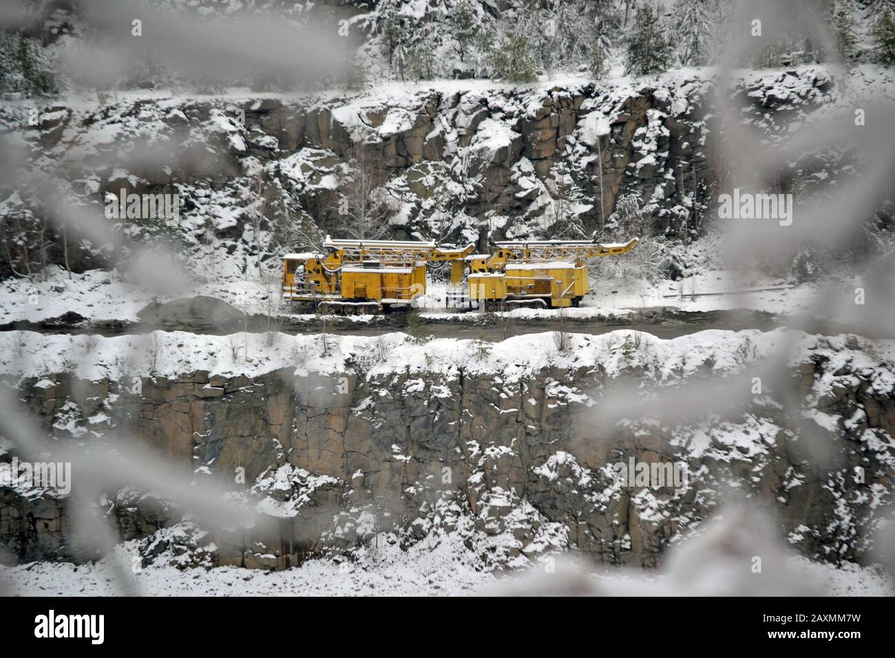 Machines d'exploitation minière jaunes sur les pentes d'une carrière de granit en hiver enneigé Banque D'Images