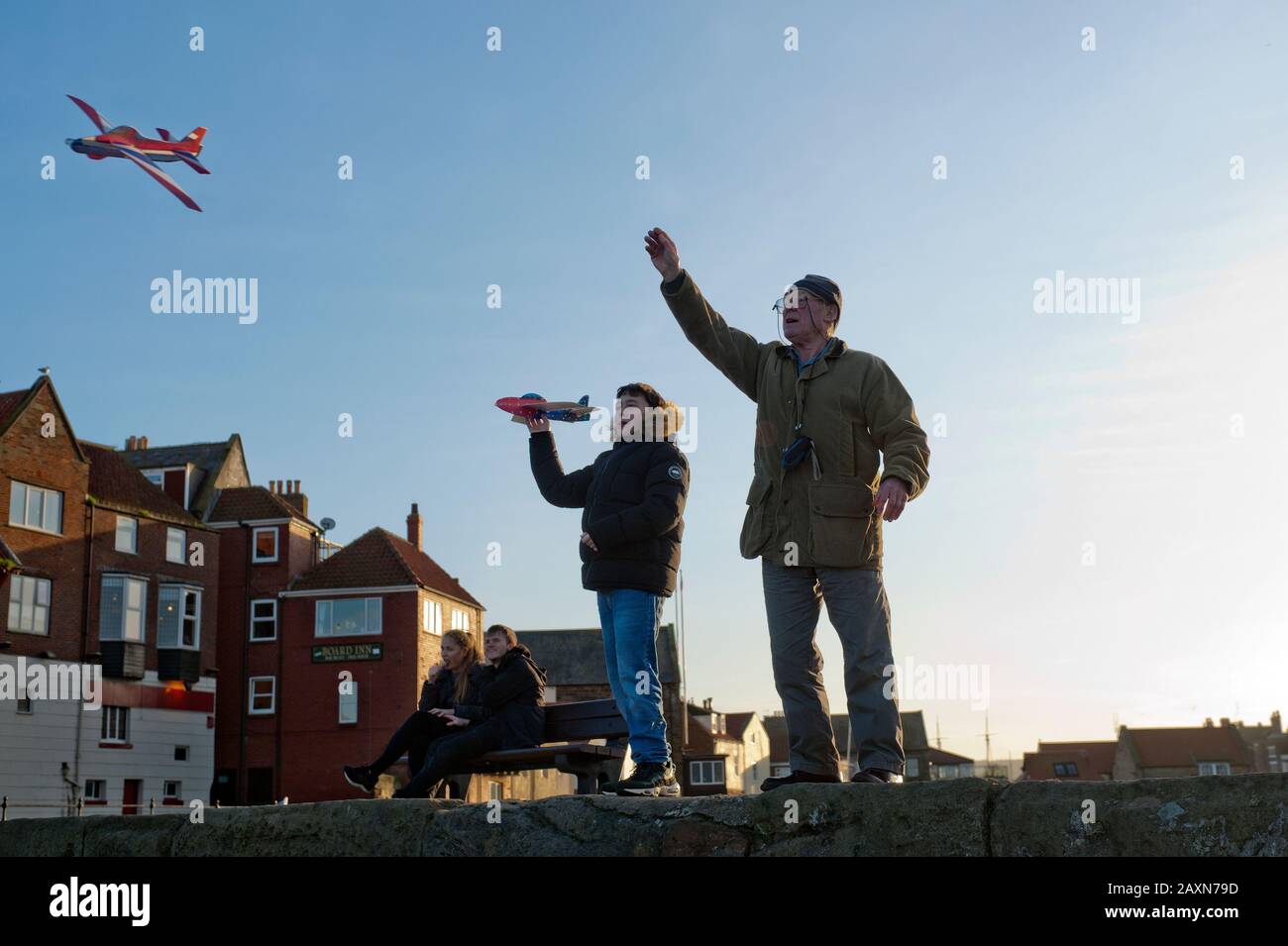 83 ans, grand-père et petit-fils d'adolescent flying paper planes ensemble off Tate Hill pier à Whitby, North Yorkshire, UK. Banque D'Images