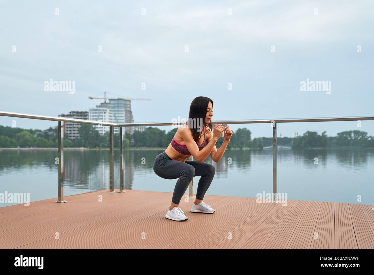 Jeune femme de fitness confiante dans un brassière, des leggings gris et des baskets blanches qui s'exercent sur la jetée pendant l'entraînement matinal régulier. Concept de mode de vie actif et sain Banque D'Images