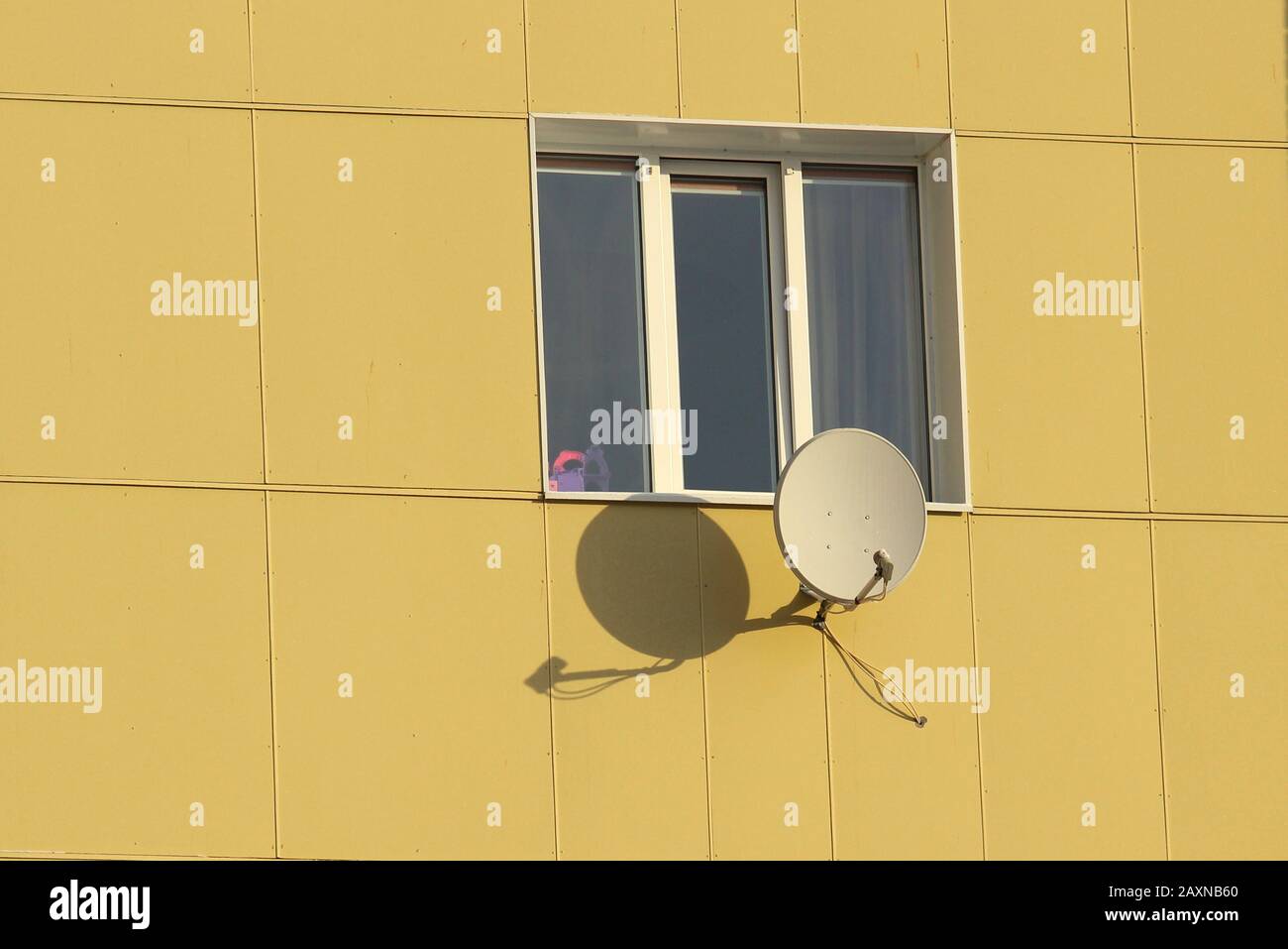 Plat satellite fixé au mur d'une maison carrelée en journée ensoleillée. Stocker la photo pour le Web et l'imprimer avec un espace vide pour le texte. Banque D'Images