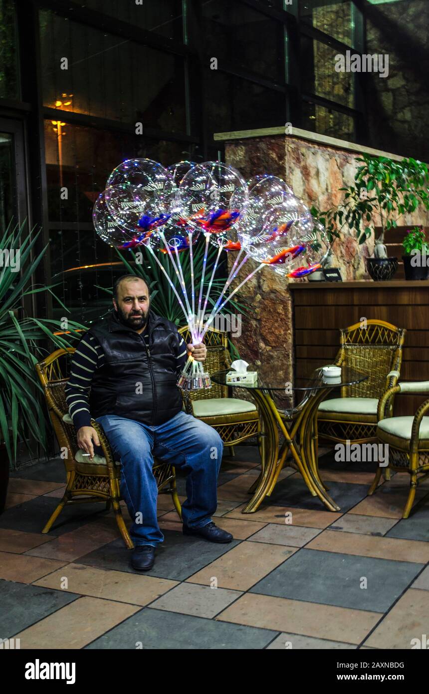 Erevan, Arménie, 02 novembre 2018 : un homme d'âge moyen vend des ballons aux lumières multicolores tout en étant assis sur une chaise dans le hall d'un restaurant Banque D'Images