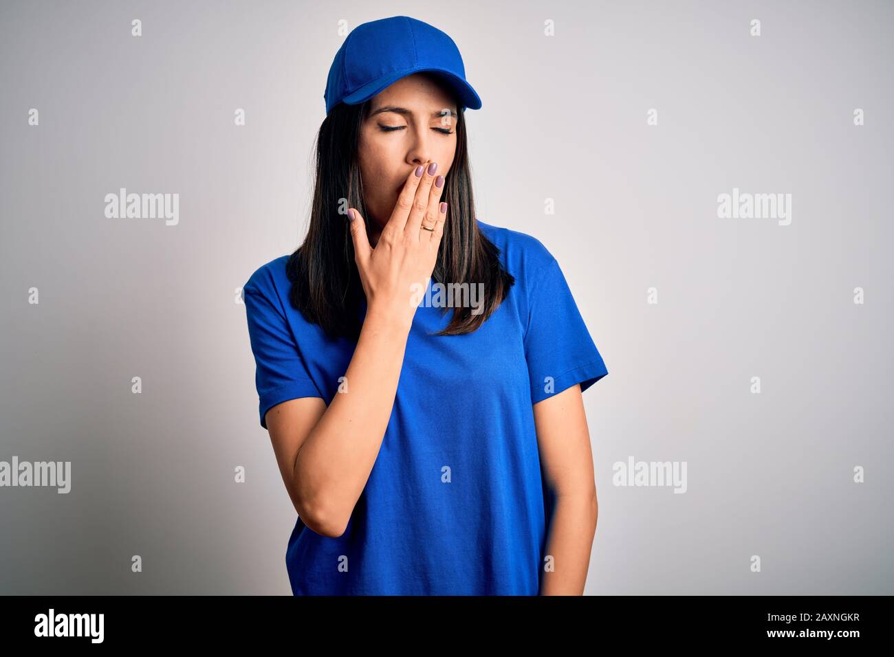 Jeune femme de livraison avec yeux bleus portant une casquette debout sur  fond bleu ennuyé bâillonner fatigué couvrant la bouche avec la main. Repos  et somnolence Photo Stock - Alamy
