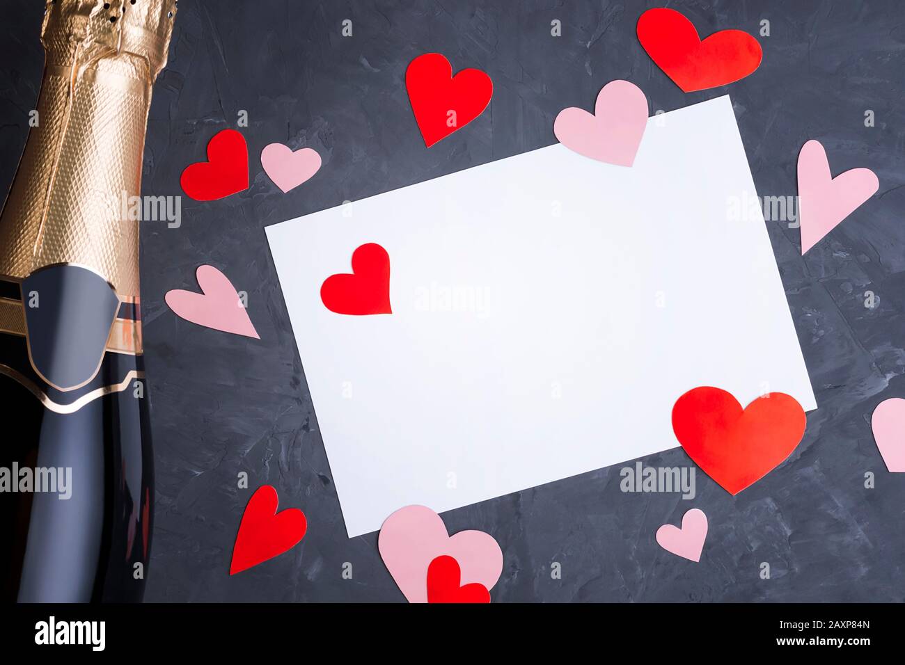 Modèle de carte de vœux Saint-Valentin à partir d'une bouteille de champagne, lettre vierge avec espace de copie et coeurs faits main rouge et rose dispersés coupés en papier Banque D'Images