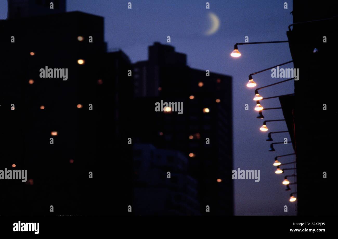 Scène nocturne avec lune de croissant, immeubles d'appartements et lumières de rue Banque D'Images